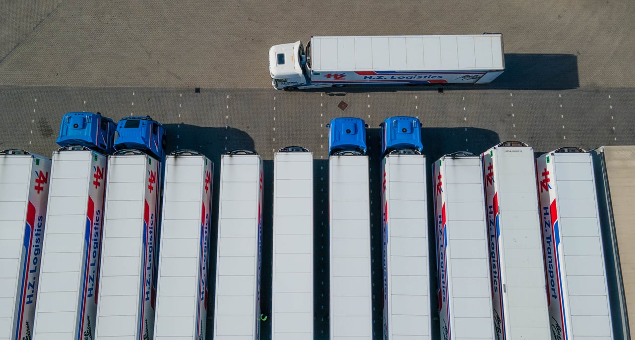 services-01 Top-down drone shot of logistics trucks arranged in a row in a parking lot.