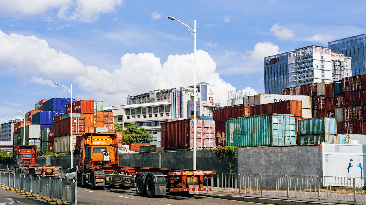 hero-img-01 Colorful shipping containers stack at an industrial port under clear skies.