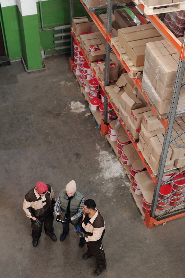 gallery-5 Group of warehouse workers discussing logistics and inventory in a large storage area with shelves and packages.